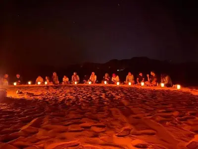 a group of people sitting on a beach at night at The sun of Wadi Rum camp in Wadi Rum
