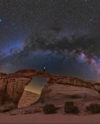 a person standing on an arch in the desert at night at Wadi Rum Desert Heart Camp in Wadi Rum