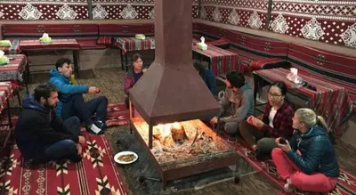 a group of people sitting around a fire in a restaurant at Wadi Rum Desert Heart Camp in Wadi Rum