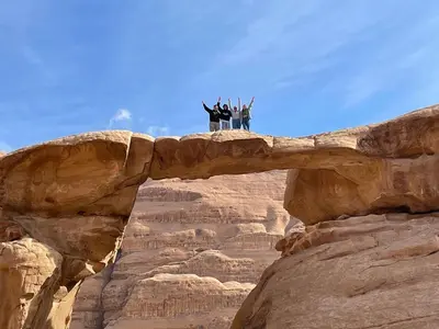 a group of people standing on a rock bridge at Jawharat Rum camp in Wadi Rum