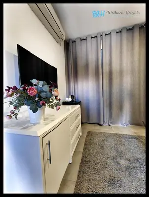 a living room with a television and flowers on a dresser at Weibdeh Heights Hotel Suites in Amman