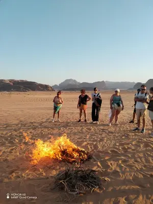 a group of people standing around a fire on the beach at Rum desert camp in Wadi Rum