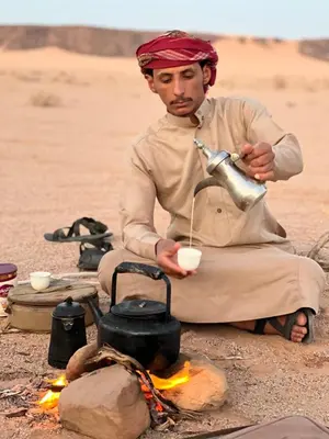 a man sitting in front of a campfire with a pot at Bedouin Desert Cave in Wadi Rum