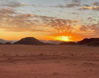a sunset in the desert with rocks in the background at Bedouin Desert Cave in Wadi Rum