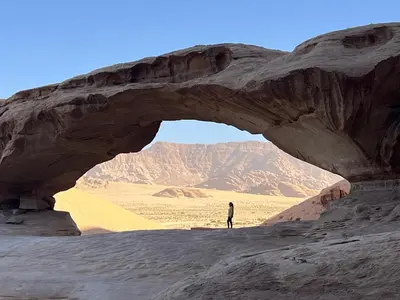 a man standing in front of an arch in the desert at Scarlet Luxury Camp Wadi Rum in Wadi Rum
