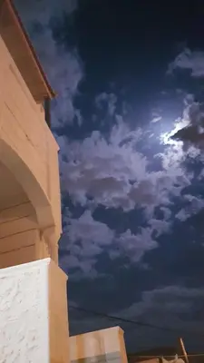 a cloudy sky with the moon behind a house at Petra Inn House in Wadi Musa