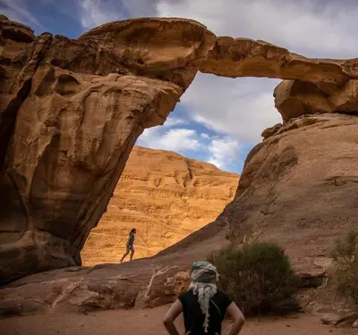 a person walking through an arch in the desert at Wadi Rum Alia Luxury Camp in Wadi Rum