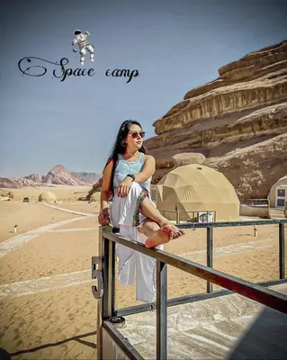 a woman sitting on a fence in the desert at Wadi Rum Space camp in Wadi Rum