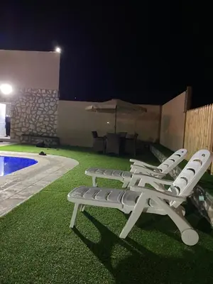 a group of lawn chairs sitting next to a pool at night at Fog Mountain Hotel Rooms & sauna in Jaḩrāʼ