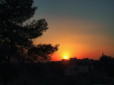 a sunset with the sun setting over a city at Beit Philodemus in Um Qeis