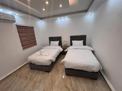 two beds in a room with white walls and wooden floors at Nabateans Home Hotel in Wadi Musa