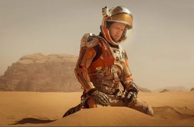 a man in an astronaut suit sitting in the desert at Star rum in Wadi Rum
