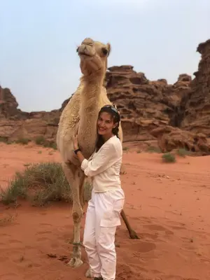a woman standing in the desert with a camel at WADi RUM LUXURY RITZ in Wadi Rum