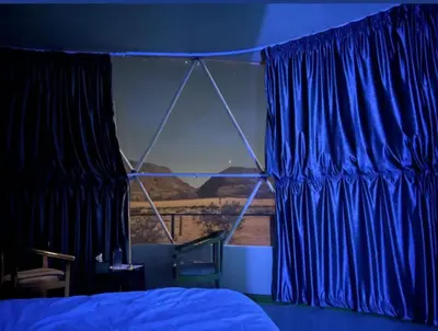 a bedroom with blue curtains and a bed and a window at Adel Wadi Rum Camp Bubble in Wadi Rum