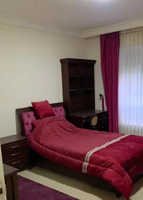 a bedroom with a red bed with a dresser and a window at Amman Business Park Apartment in Amman