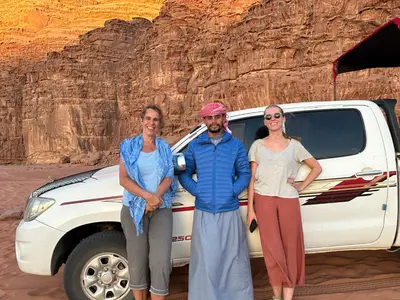 three people standing in front of a truck in the desert at Wadi Rum Khalifa Camp in Wadi Rum