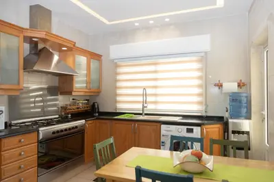 a kitchen with wooden cabinets and a table and a sink at Hanan Residence 01 - 3BR, Der Ghbar 165m2 in Amman