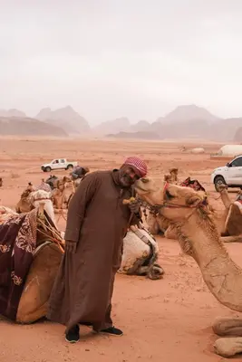 a man standing next to a group of camels in the desert at Shaheen Camp Wadi rum in Wadi Rum