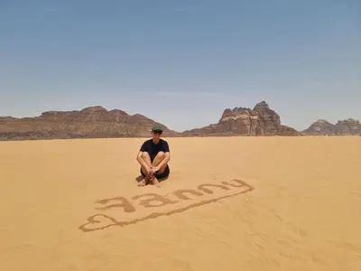 a man sitting in the desert with a sign in the sand at Mahmmad Luxury Camp in Wadi Rum