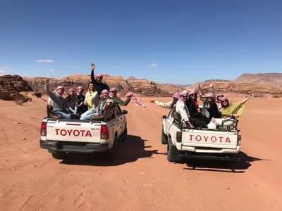 a group of people riding in the back of toyota trucks in the desert at Wadi rum Wild life camp in Wadi Rum