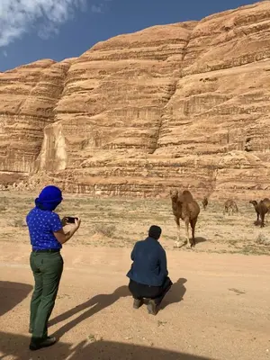 two people are taking pictures of a camel in the desert at Wadi Rum Cream in Wadi Rum