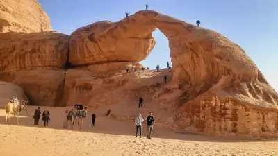 a group of people walking in front of a rock formation at Wadi Rum Cream in Wadi Rum