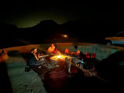 two people sitting around a fire in the sand at night at Wadi rum view camp in Wadi Rum