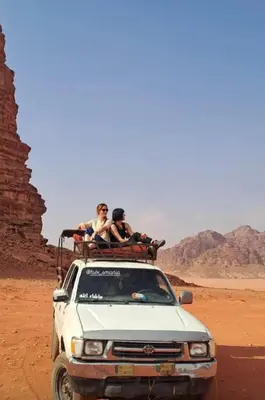 three people sitting on the roof of a truck in the desert at Wadi rum view camp in Wadi Rum
