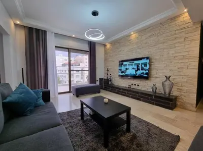 a living room with a couch and a tv on a brick wall at Deir Ghbar 3 rooms apart in Amman