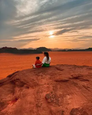 a woman and child sitting on a rock in the desert at Wade rum natural in Wadi Rum
