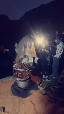 a group of people standing around a grill with food at blueskyrum. in Wadi Rum