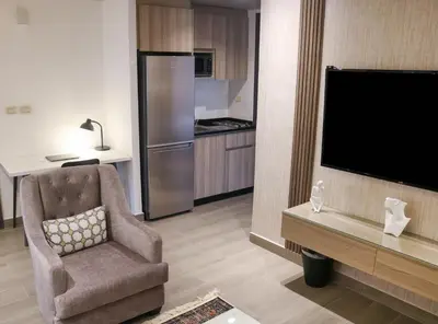 a living room with a tv and a chair and a kitchen at Red Carpet Hotel & Suites in Amman