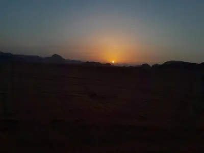 a sunset in a field with the sun setting in the distance at Desert Star of Wadi Rum in Wadi Rum