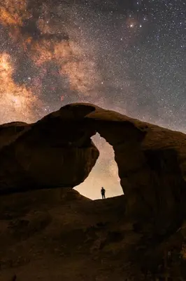 a person standing under an arch under the milky way at Whispering Rum in Wadi Rum