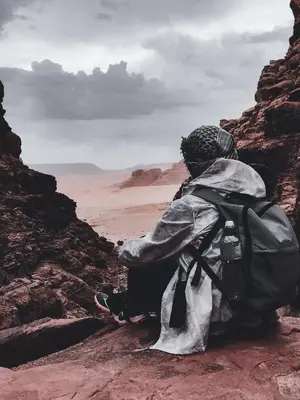 a person with a backpack sitting on the rocks looking at the desert at Whispering Rum in Wadi Rum