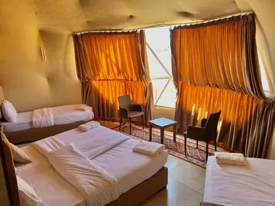 a room with three beds and chairs and a window at Whispering Rum in Wadi Rum
