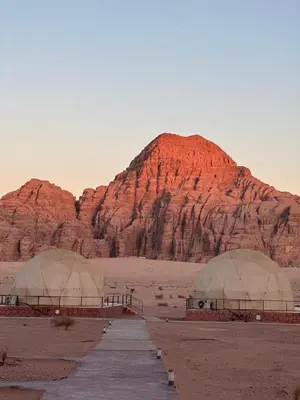 two domes in the desert with a mountain in the background at Hakon Matata Wadi Rum Jeep Tours Camp in Wadi Rum