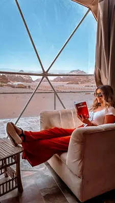 a woman sitting on a couch reading a book at LARA lUXURY CAMP in Wadi Rum