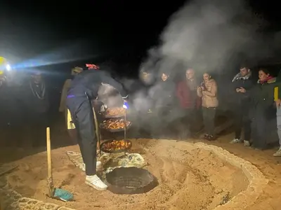 a man cooking food over a grill in the dirt at wadirumtours&camp in Wadi Rum