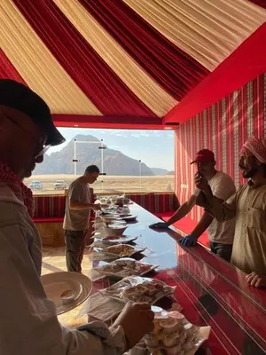 a group of people standing around a long table with food at Wadi Rum Gulf camp in Aqaba