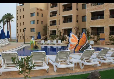 a group of lounge chairs and a swimming pool in front of a building at Dead Sea view Elite apartment Samara Resort traveler award 2024 in Sowayma