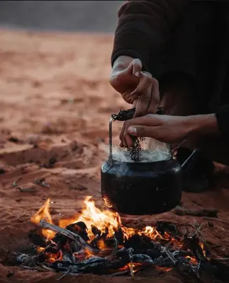 a person cooking food in a pot over a fire at Wadi Rum alsultan Camp in Wadi Rum